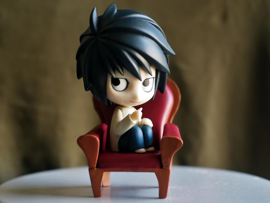 An action figure of L, the character from the anime, Death Note, sitting in a red sofa